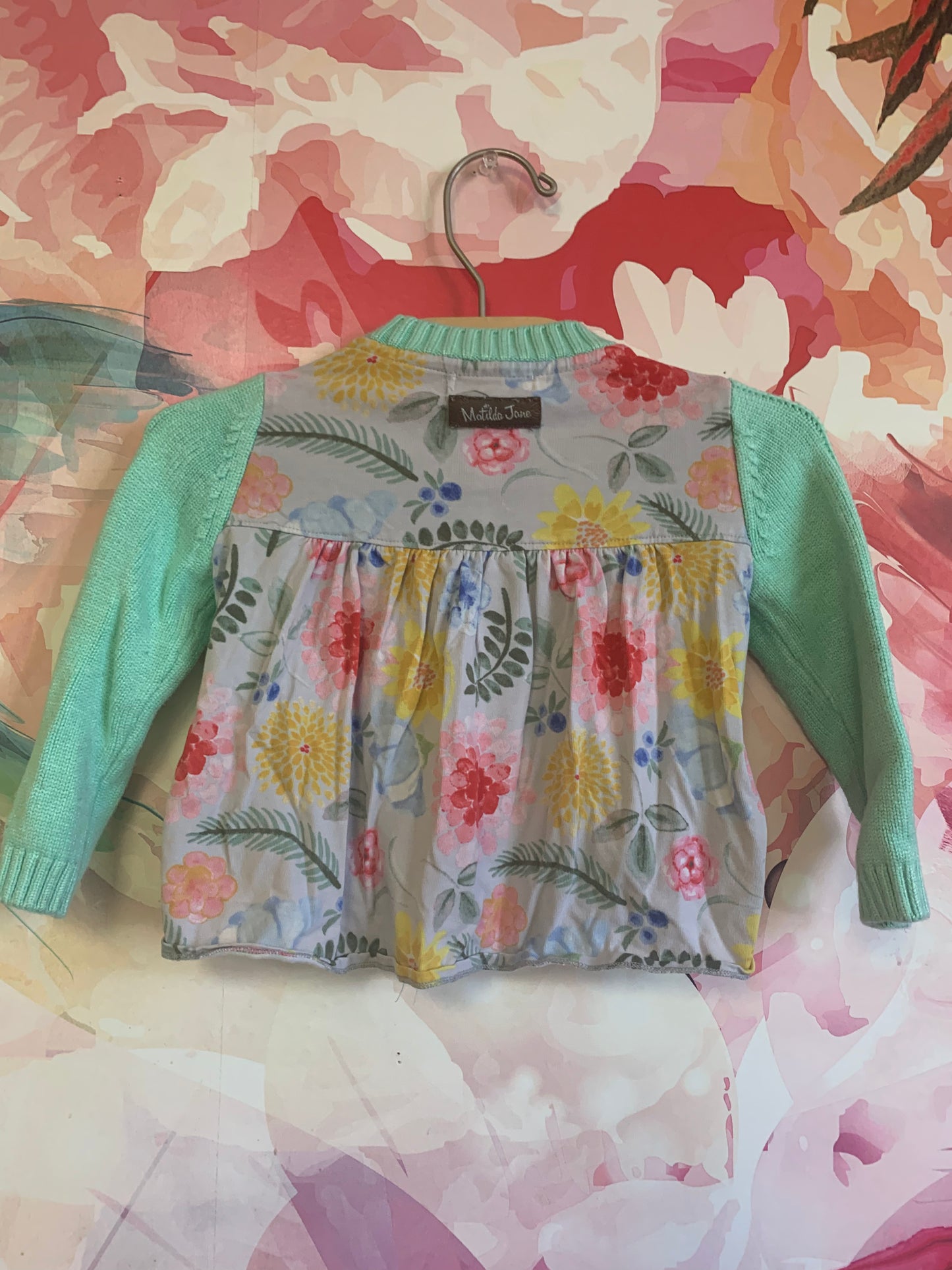 Matilda Jane green cardigan with colorful floral ruffles on front and back of sweater. Wooden buttons and two front pockets. Size 12-18m