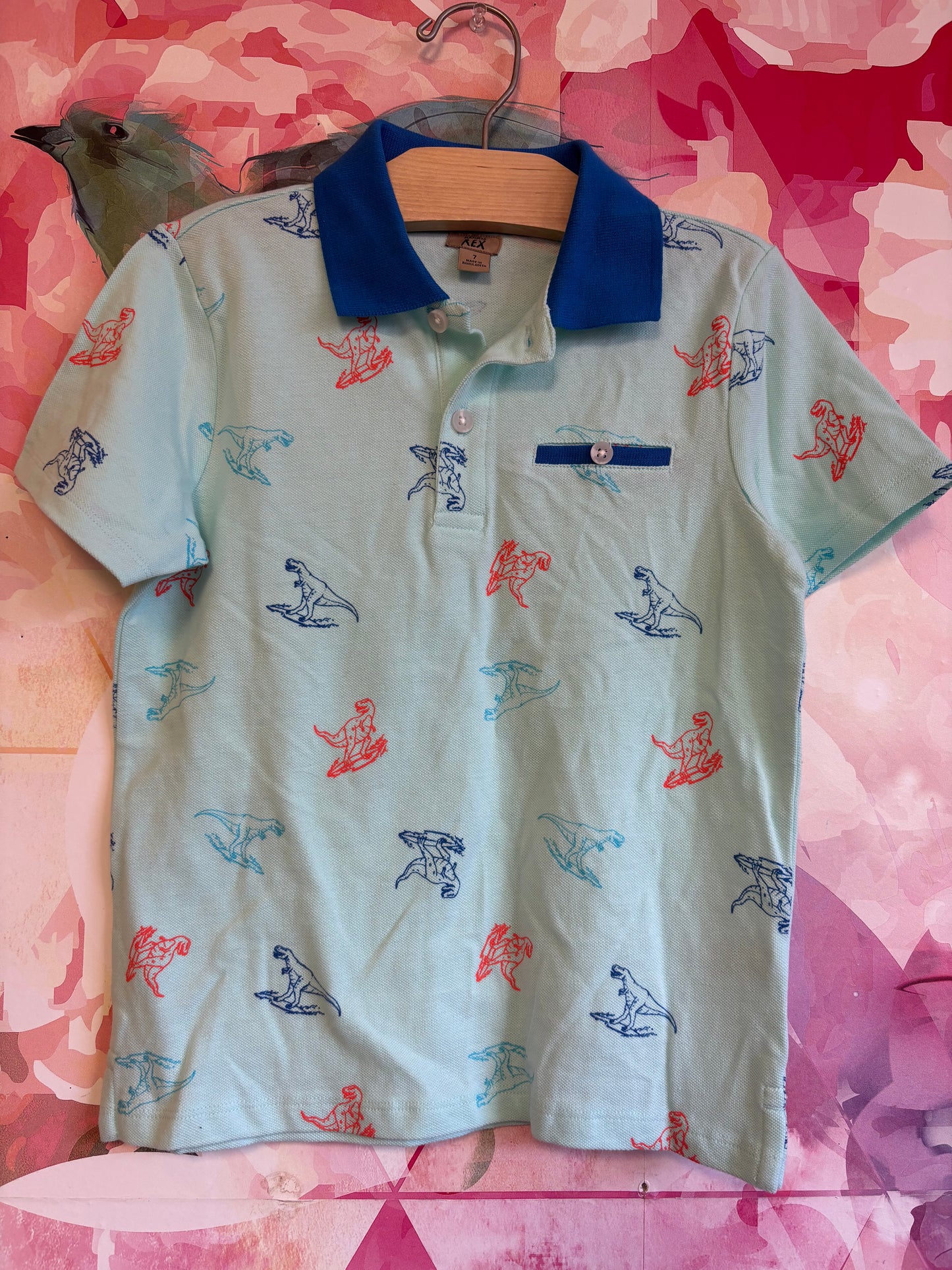 Maximus Rex light blue short sleeve polo with orange and blue dinosaur outlines. Size 7.