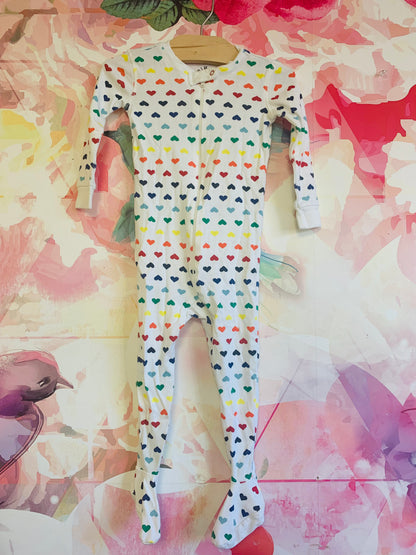 Primary white long sleeve footed romper with rainbow hearts. Grippers on soles of feet. Size 12-18m