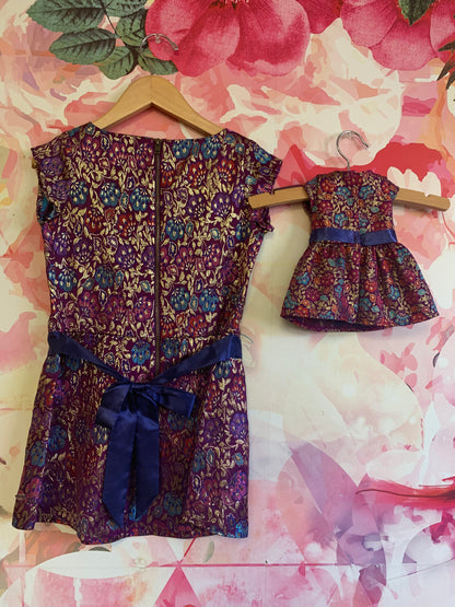 American Girl purple short sleeve dress with fuschia, red, blue, gold flowers & blue waist sash. Zipper back. Size 6. Includes Matching dress for doll. NEW WITH TAGS